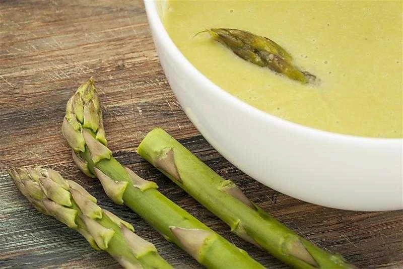 Crock Pot Cream Of Asparagus Soup in white bowl with aspargus tip in it on table