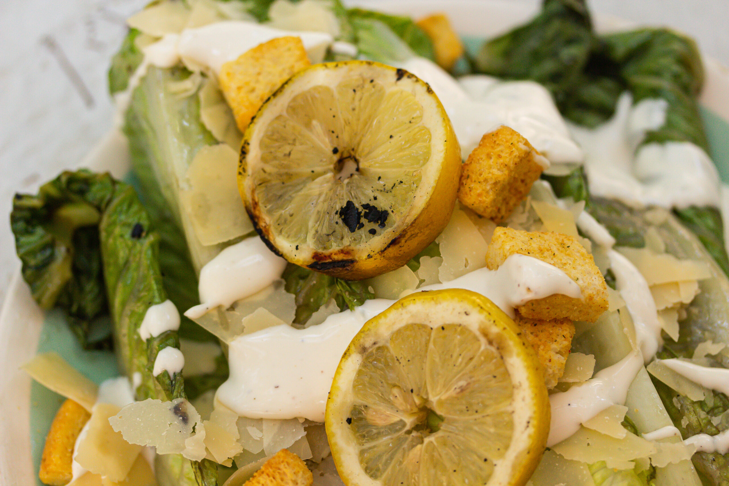 close up of grilled caeser salad with grilled lemons on blue background