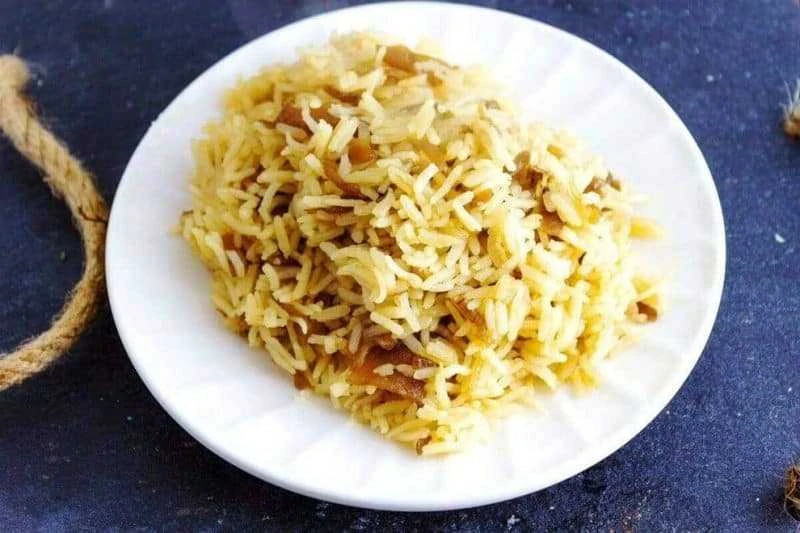 Close up of French Onion Rice on a white plate on dark slate and a rope