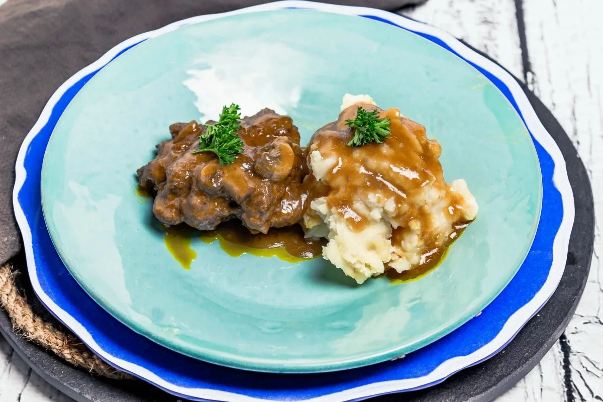 Slow Cooker Salisbury Steak is made with a rich, tangy gravy that is made in the slow cooker and is perfect for a busy family dinner! Slow Cooker Salisbury Steak wide view on plate