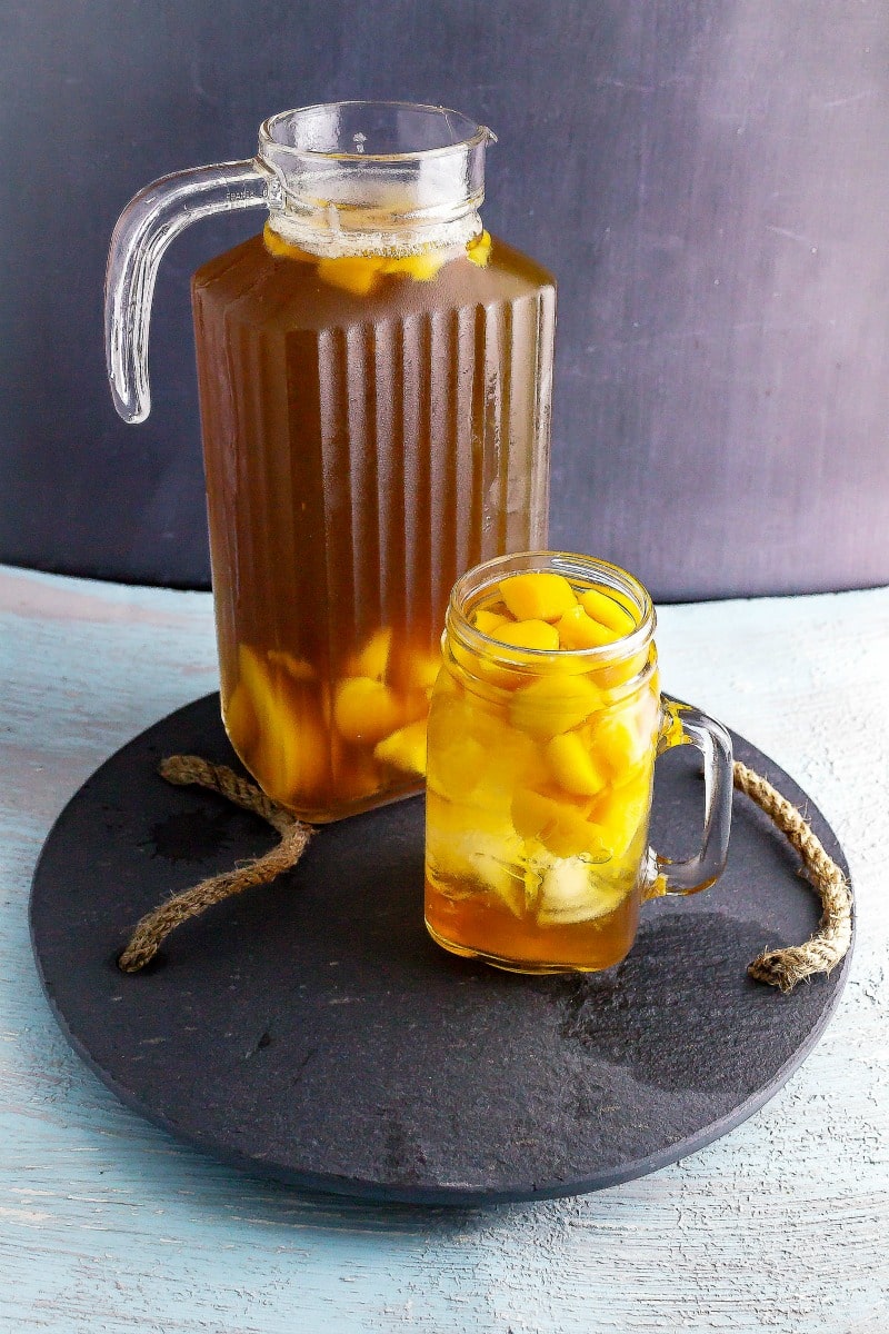 Pitcher of peach sweet tea on slate with glass of iced tea