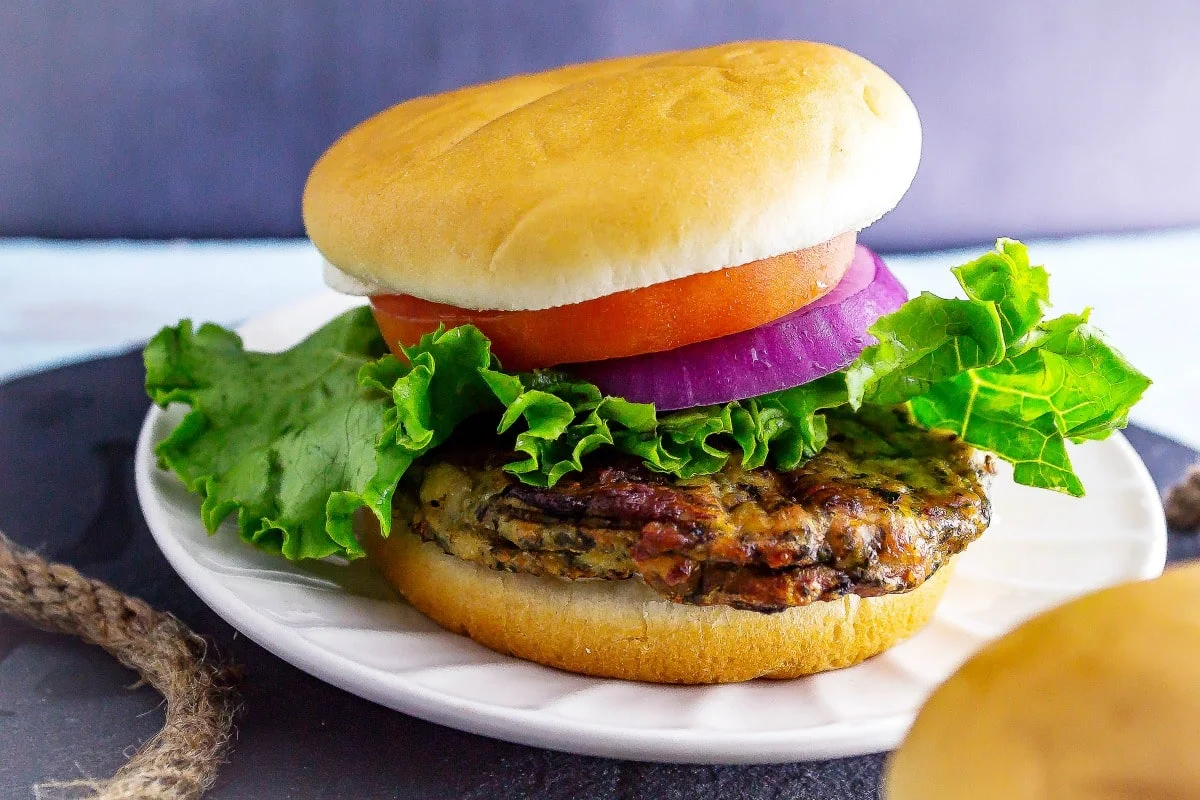 Greek Spinach and Feta Chicken Burgers are a tasty Greek-inspired low fat chicken burger recipe. These healthy chicken burgers are made with ground chicken. Greek Spinach and Feta Chicken Burgers on white plate and serving tray