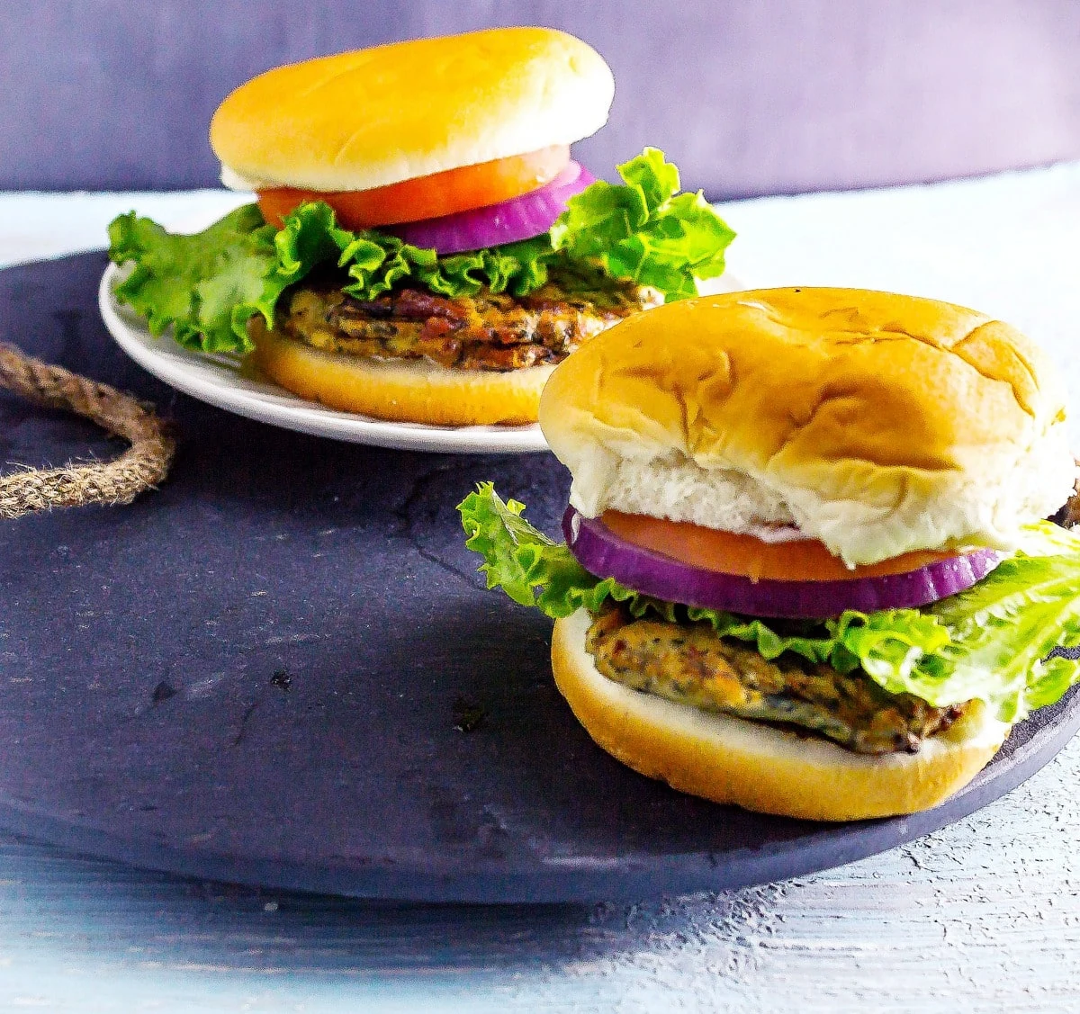 Greek Spinach and Feta Chicken Burgers are a tasty Greek-inspired low fat chicken burger recipe. These healthy chicken burgers are made with ground chicken. 2 Greek Spinach and Feta Chicken Burgers on slate serving tray on table
