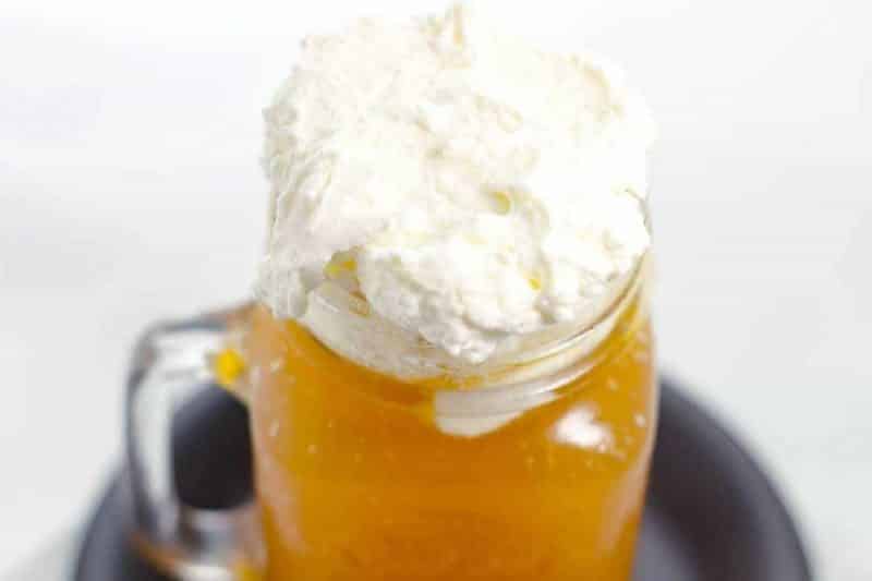 Top view of Butterbeer in a mason jar mug with whipped foam topping on black plate