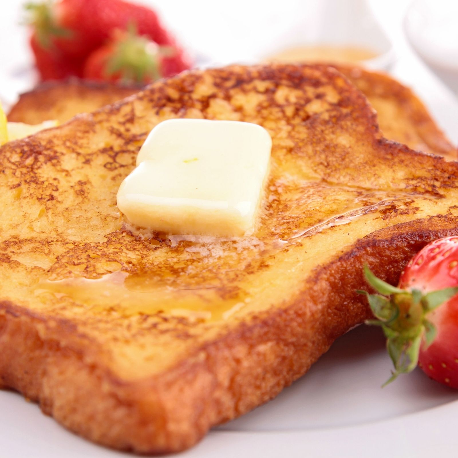 French toast with butter and strawberries on white plate