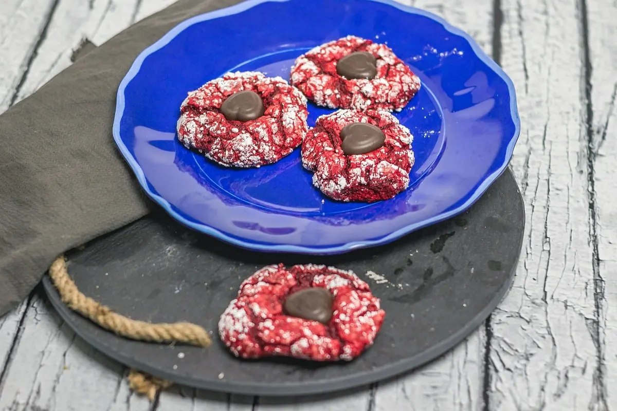 Valentine Red Velvet Cake Mix Blossoms are easy to make and is 5 ingredients! It combines the crinkle cookie with a blossom cookie for a yummy Valentine's Day Treat! Valentine Red Velvet Cake Mix Blossoms on table wide view cookies on plate