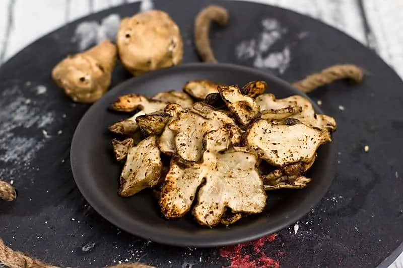 Baked Rosemary And Olive Oil Sunchoke Chips is a healthier alternative to baked potato chips! These nutty flavored baked chips have a great taste with the rosemary salt that flavors this snack Baked Rosemary And Olive Oil Sunchoke Chips on black plate
