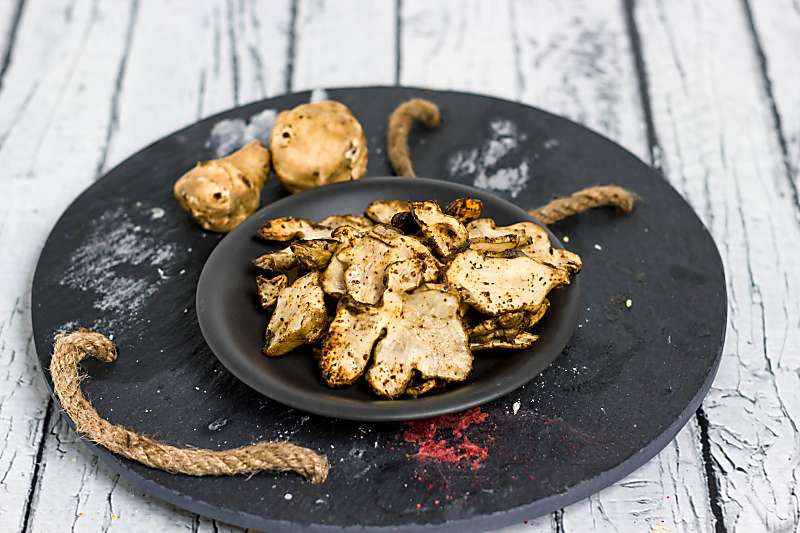 Baked Rosemary And Olive Oil Sunchoke Chips long view on table on black plate