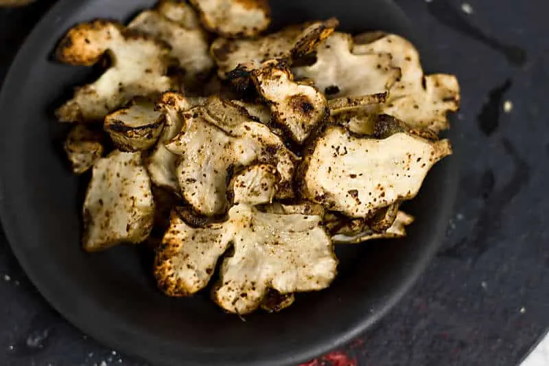 Baked Rosemary And Olive Oil Sunchoke Chips is a healthier alternative to baked potato chips! These nutty flavored baked chips have a great taste with the rosemary salt that flavors this snack Baked Rosemary And Olive Oil Sunchoke Chips overhead view chips on black plate