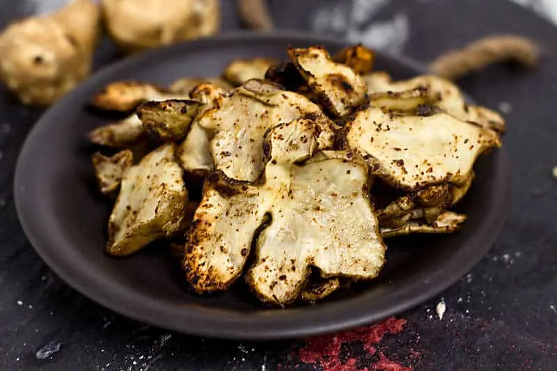 Baked Rosemary And Olive Oil Sunchoke Chips is a healthier alternative to baked potato chips! These nutty flavored baked chips have a great taste with the rosemary salt that flavors this snack Baked Rosemary And Olive Oil Sunchoke Chips close up on black plate