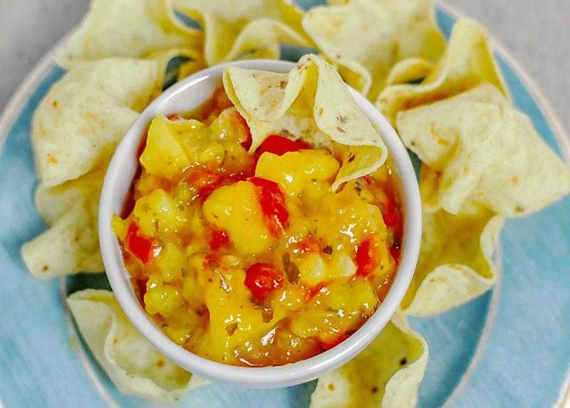 Mango salsa in white bowl on table with chips on blue plate