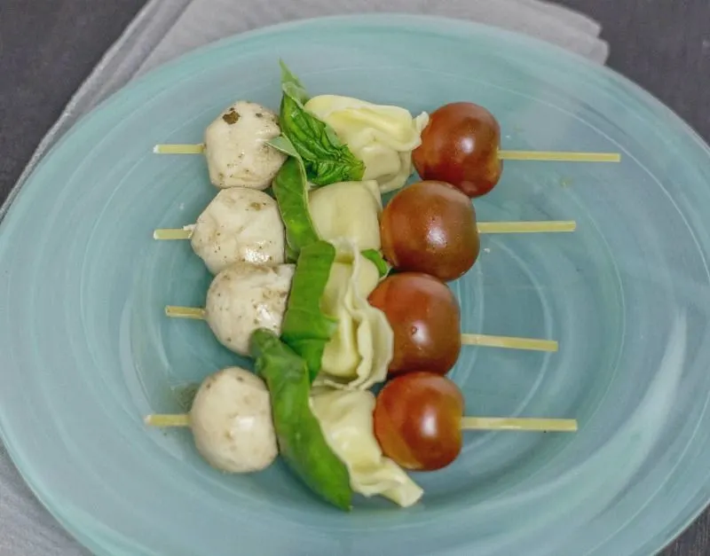 Tortelini Caprese skewer s on a blue glass plate