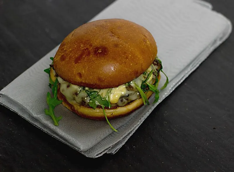 Pesto Portabello Chicken Burger on a silver table cloth on black table wide shot