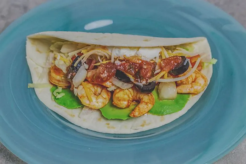 Avocado on the bottom, shrimp on top soft shell shrimp taco on blue plate close up