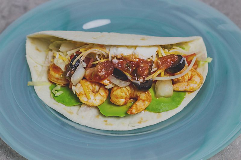 Shrimp with avocado, cheese, harissa sauce on soft shell taco on blue plate