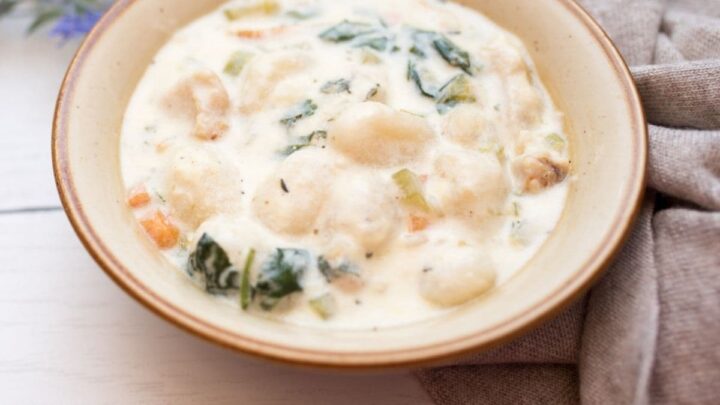 Slow Cooker Gnocchi Chicken Soup in a beige bowl with brown specks on white wood table