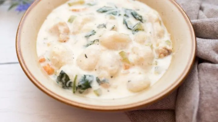 Slow Cooker Gnocchi Chicken Soup in a beige bowl with brown specks on white wood table