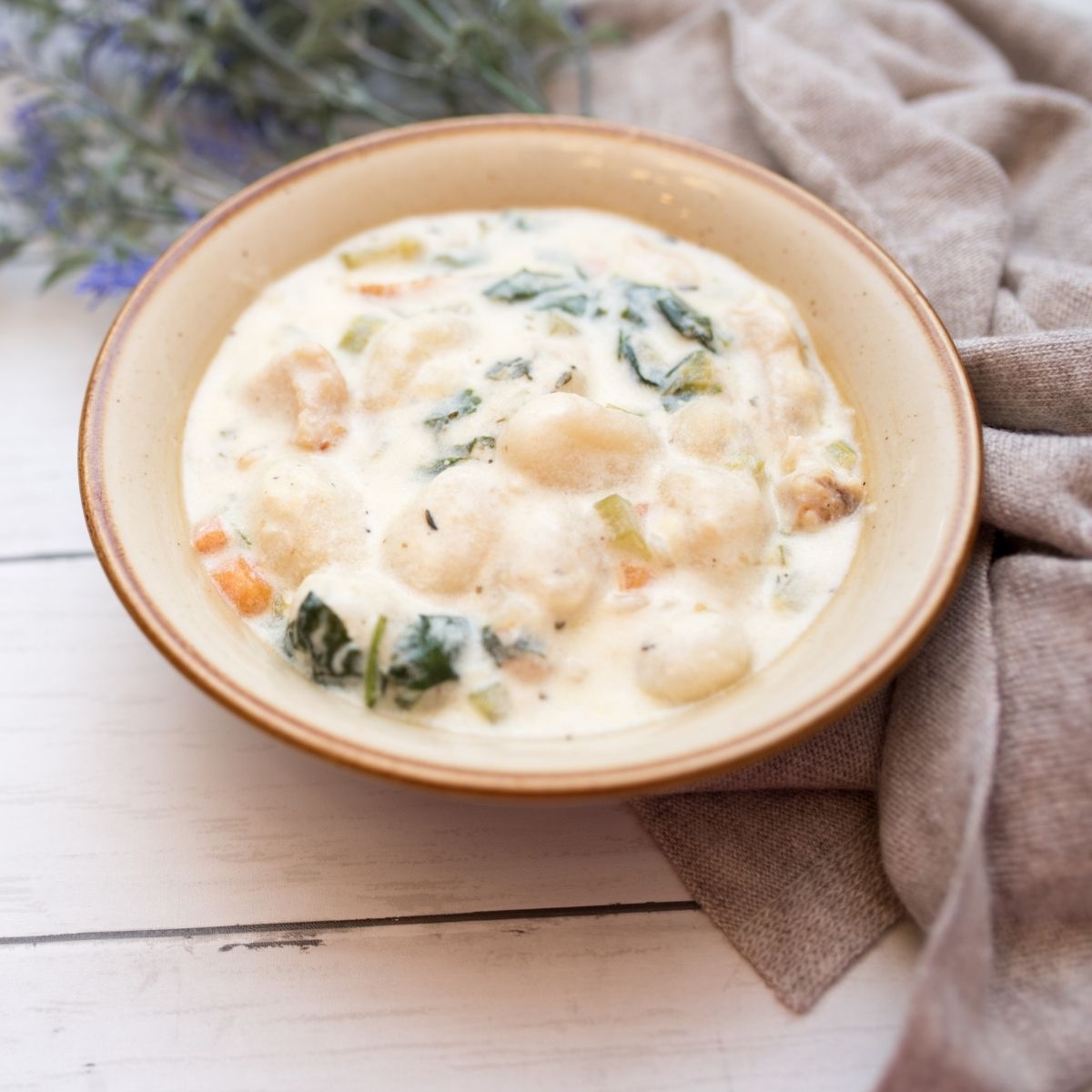 Slow Cooker Gnocchi Chicken Soup in a beige bowl with brown specks on white wood table