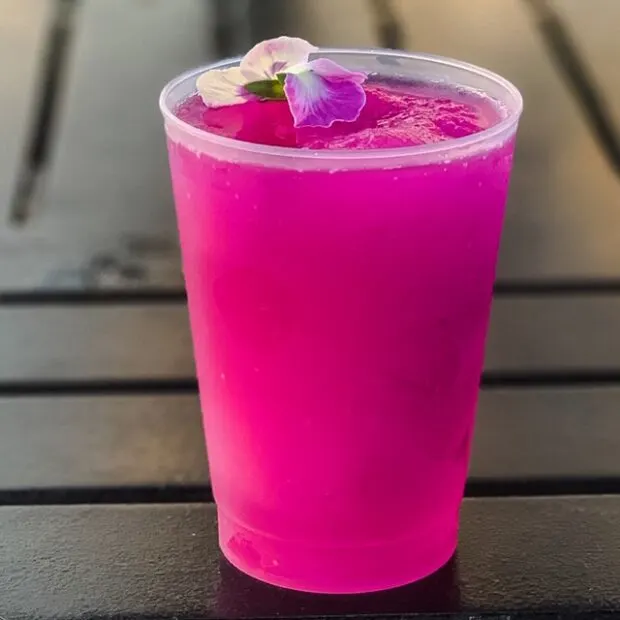 violet lemonade in clear cup with violet on top on black table