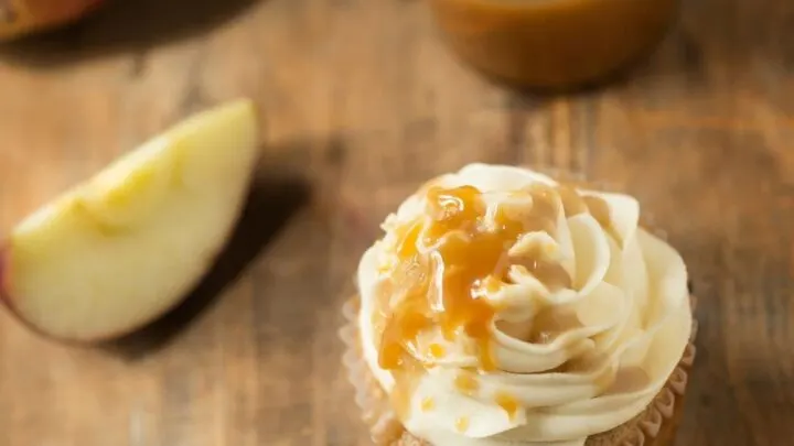 Apple Pie Cupcakes with Caramel Buttercream Apple Pie Cupcakes with Caramel Buttercream with white cupcake liner on white napkin on wood table wide view