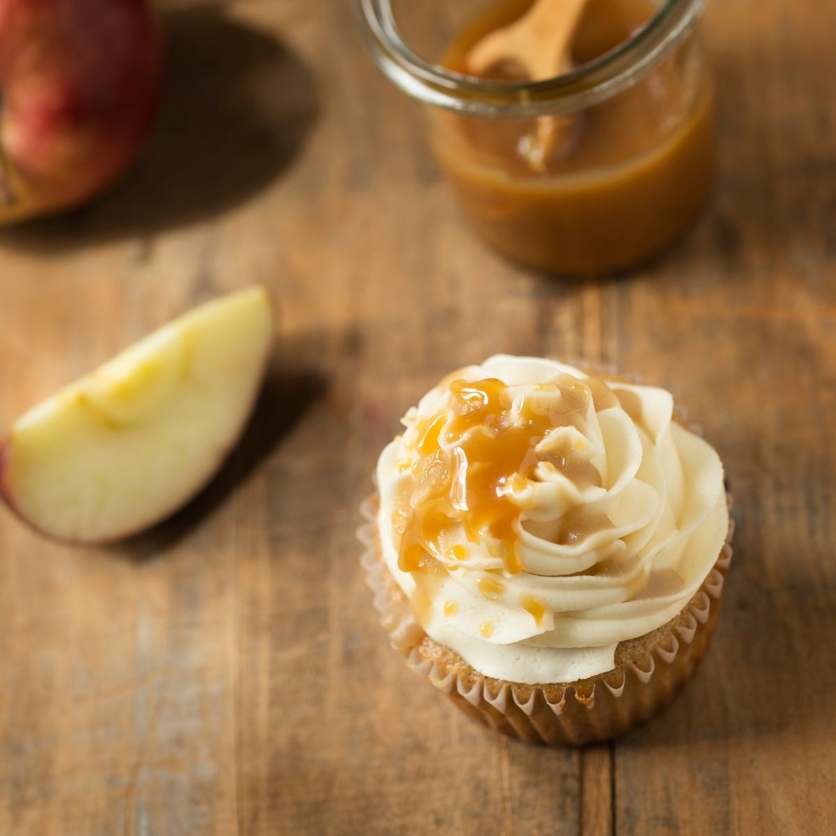 Apple Pie Cupcakes with Caramel Buttercream with white cupcake liner on white napkin on wood table wide view
